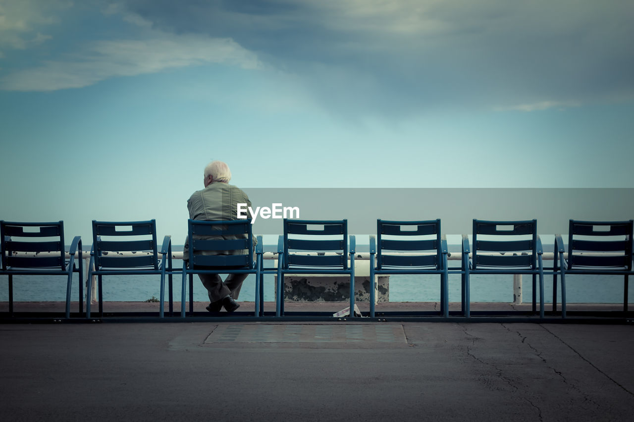 Rear view of man sitting on chair against cloudy sky