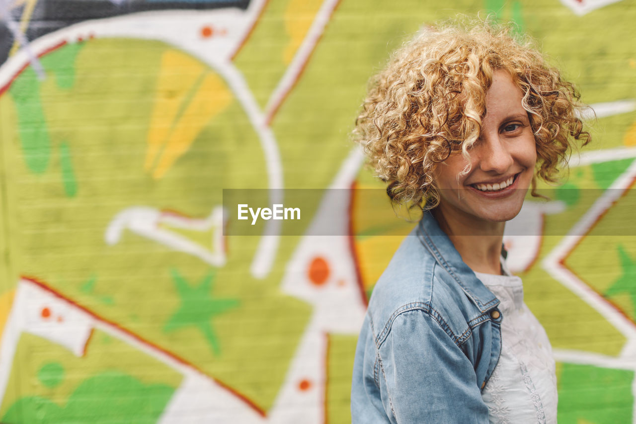 Portrait of happy woman against graffiti on wall