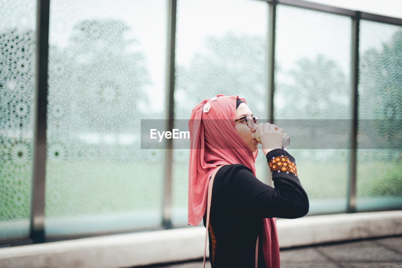 Woman drinking while standing by window