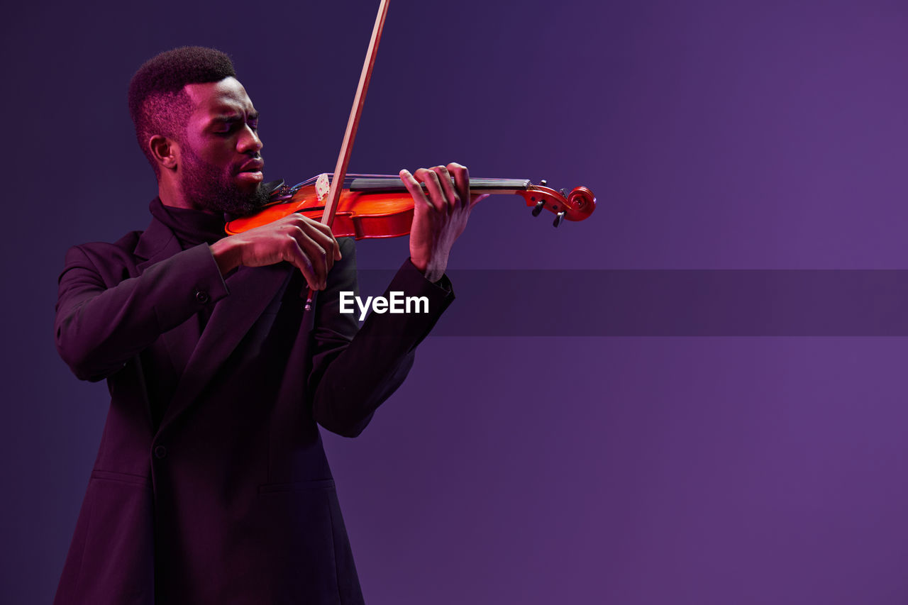 cropped image of man holding violin against clear blue sky