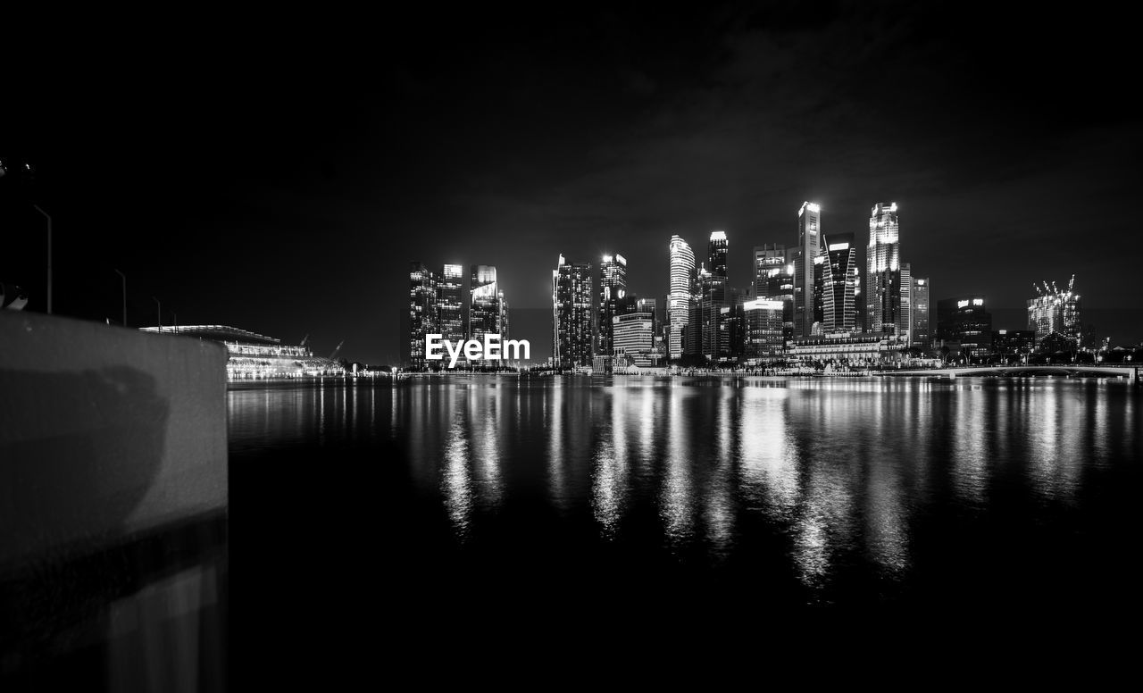 Illuminated city by river against sky at night