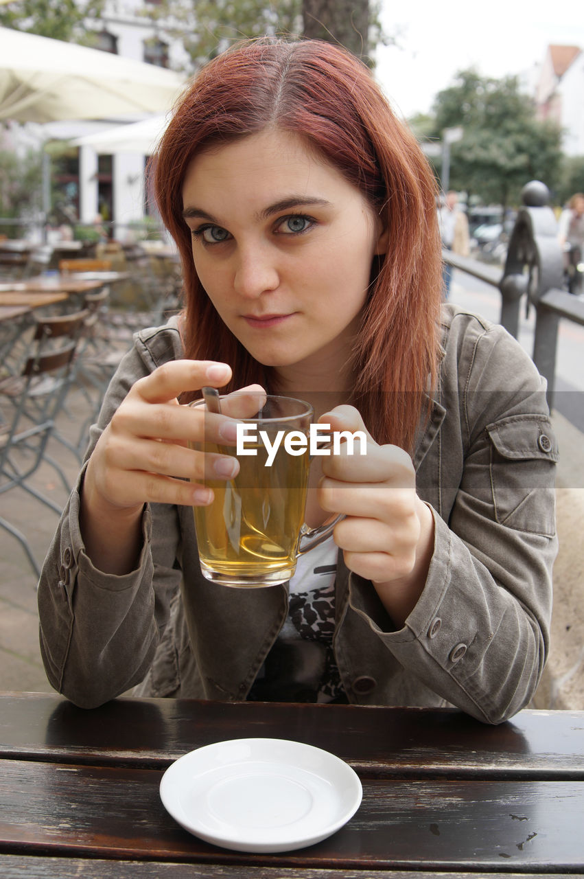 Young woman having drink while sitting at outdoor cafe