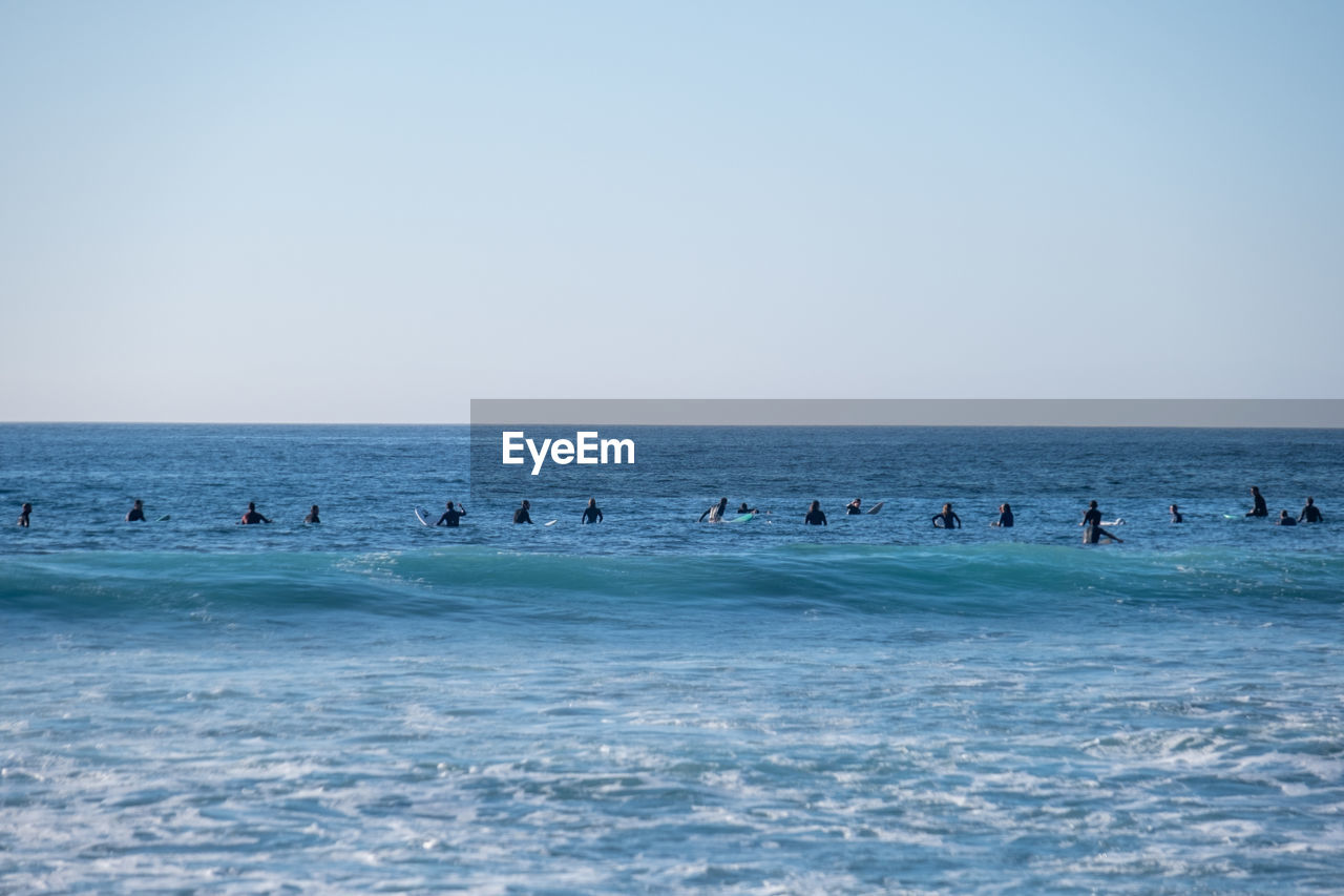 People swimming in sea against clear sky