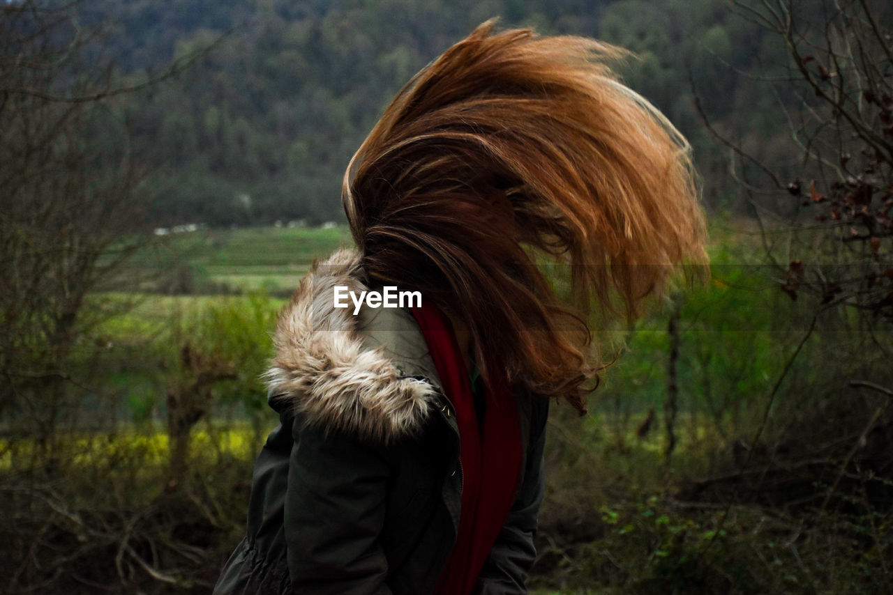 Young woman tossing hair while standing on field against trees