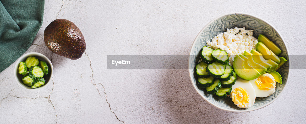 Fresh cottage cheese, avocado, cucumber and boiled egg in a plate top view web banner