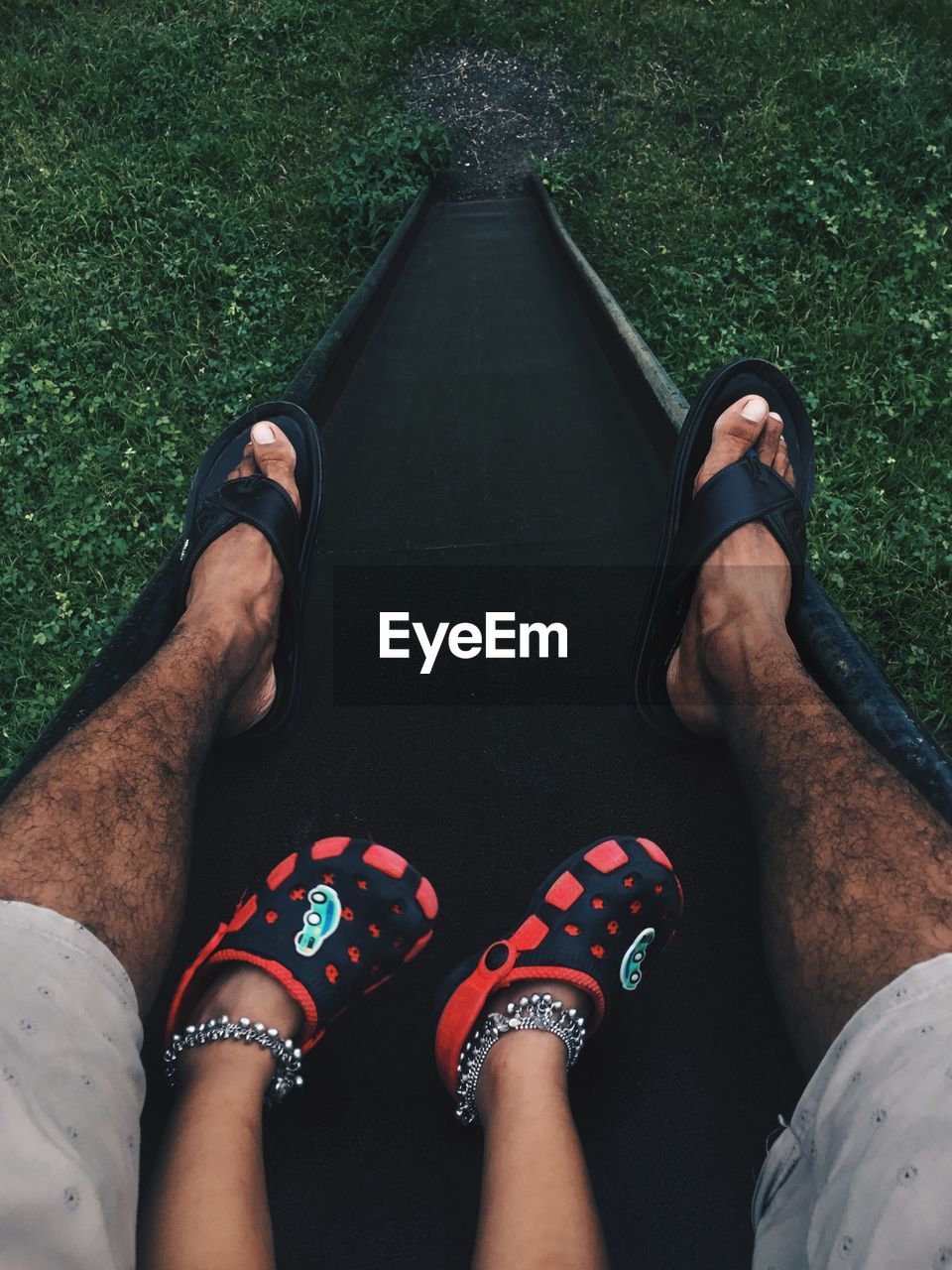 Low section of father and daughter on slide in playground