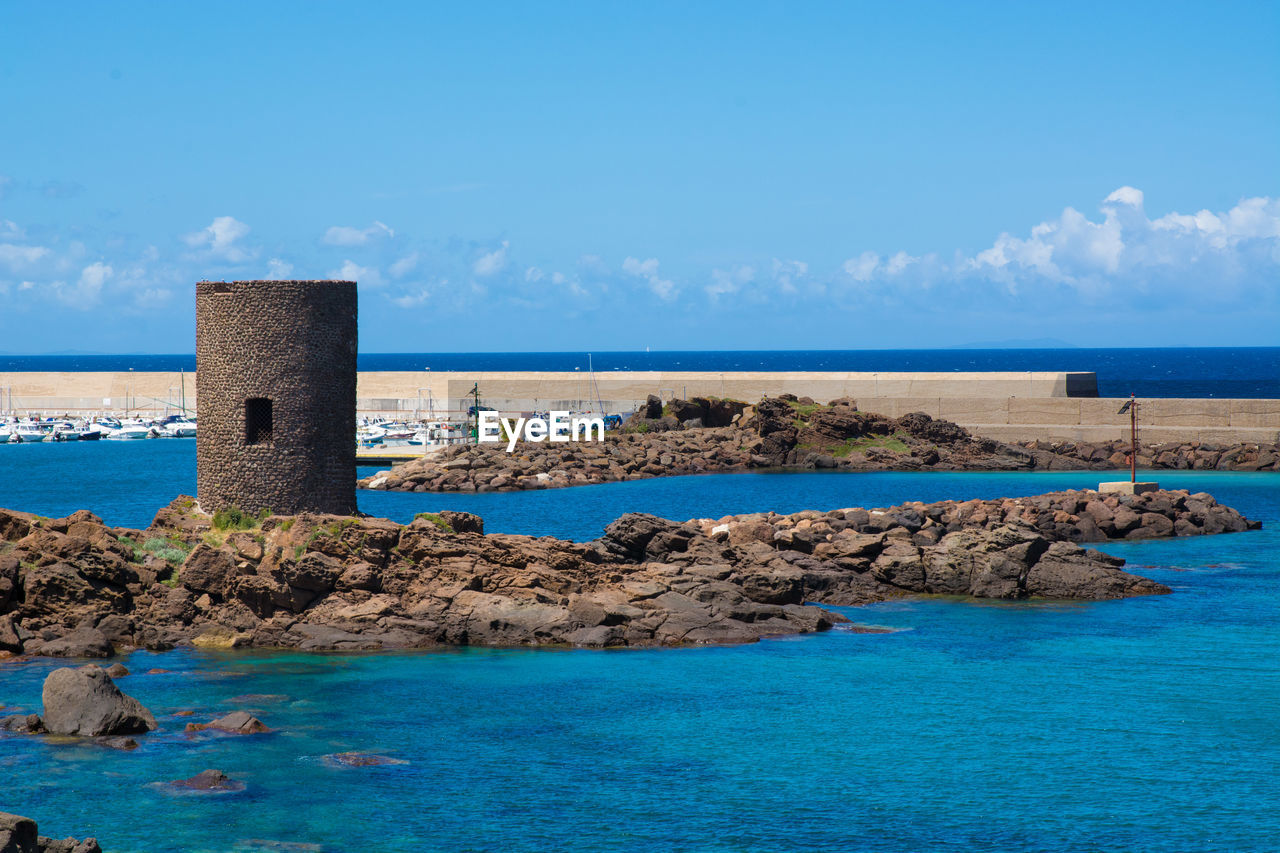 Tower amidst sea against sky at castelsardo