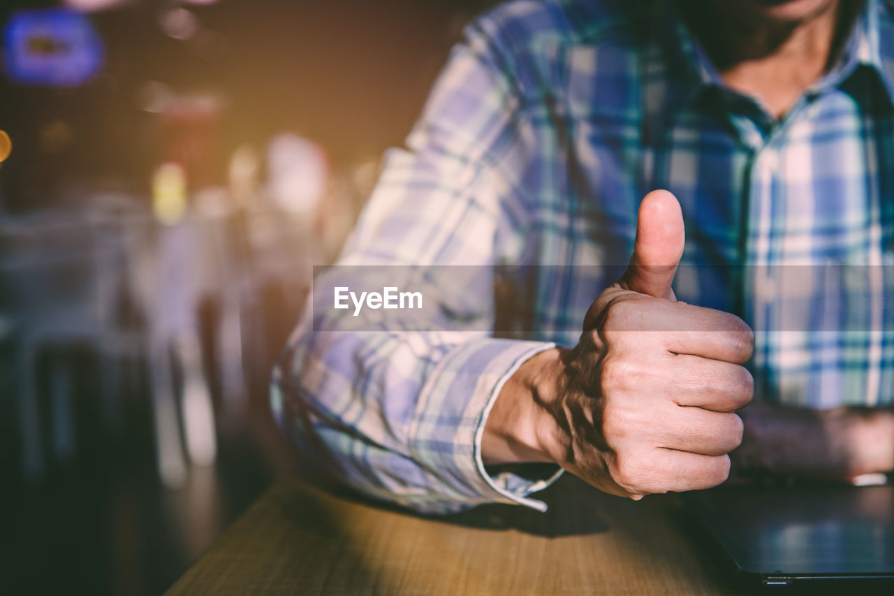 Midsection of man gesturing thumbs up while sitting at table