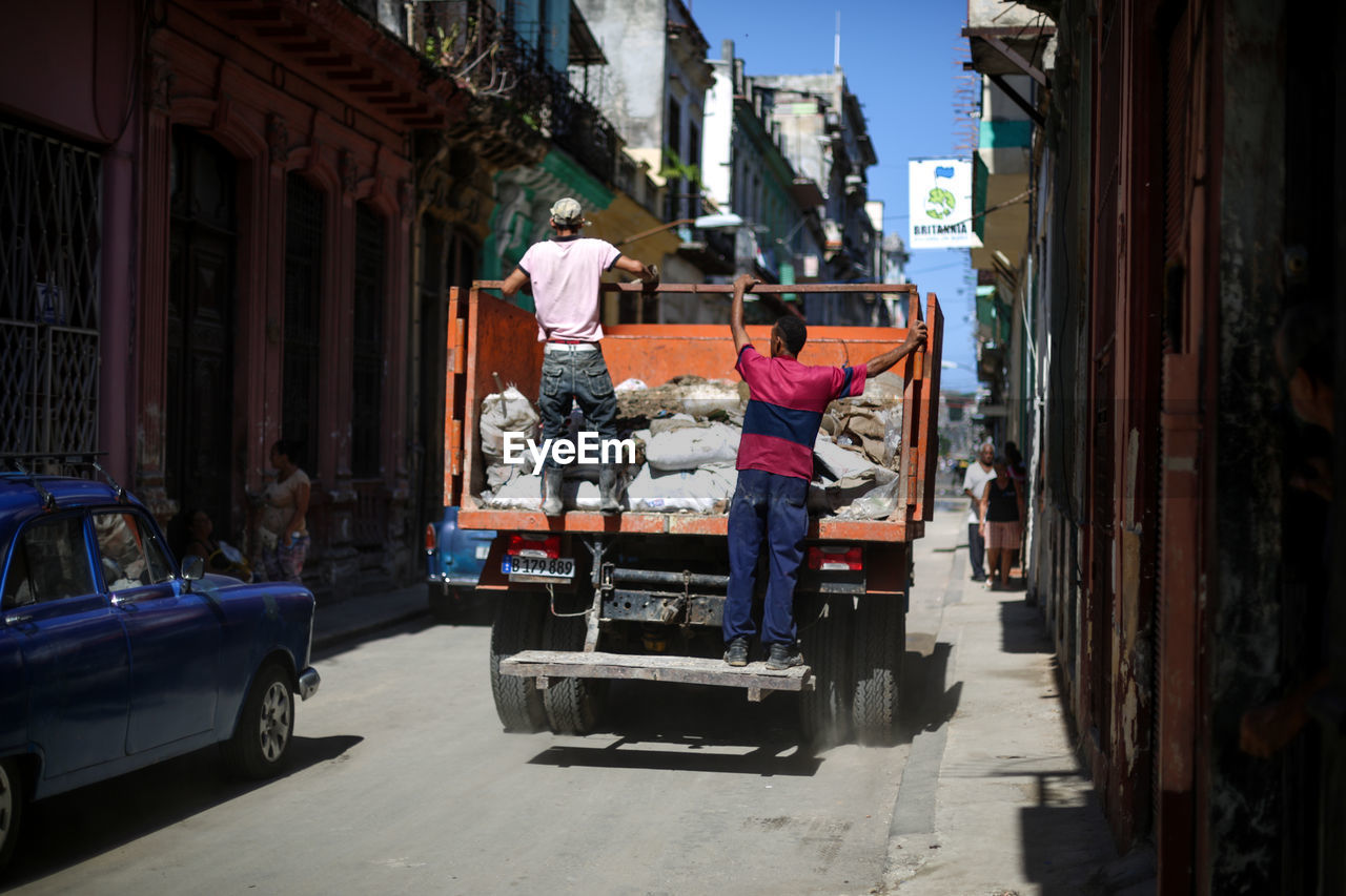 Rear view of men on garbage truck at city street