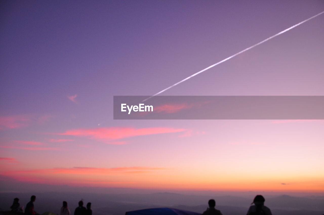 Silhouette people standing against vapor trail in sky during sunset