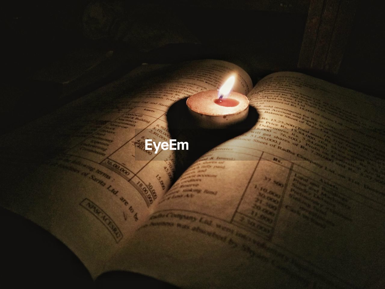 Close-up of lit tea light on open book in dark