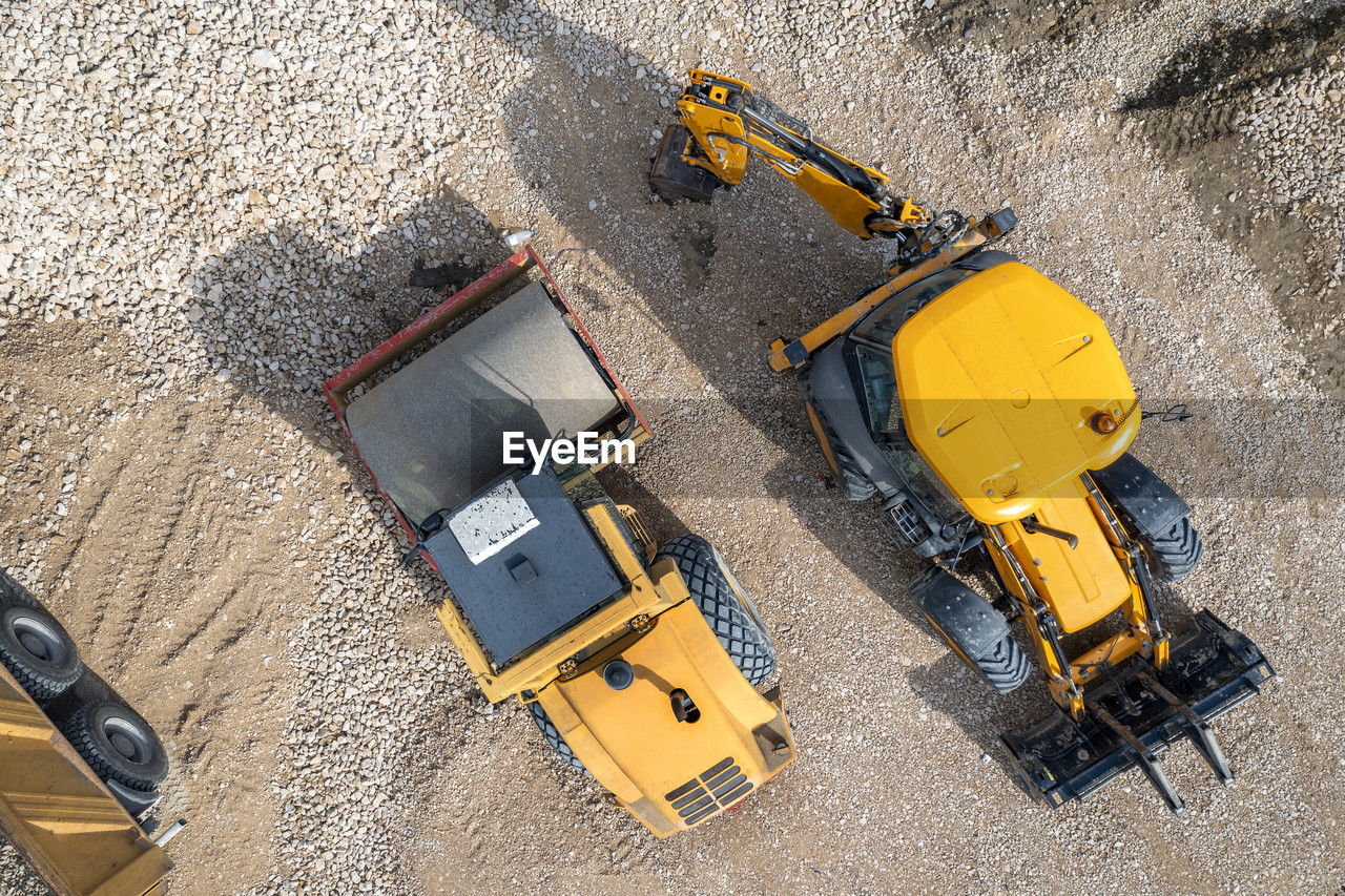 Aerial view of the stopped yellow excavator and drum roller at a construction site