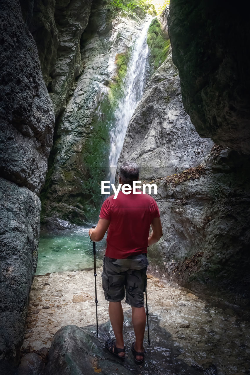 A hiker in the gorge surrounded by rocks in front of the waterfall.