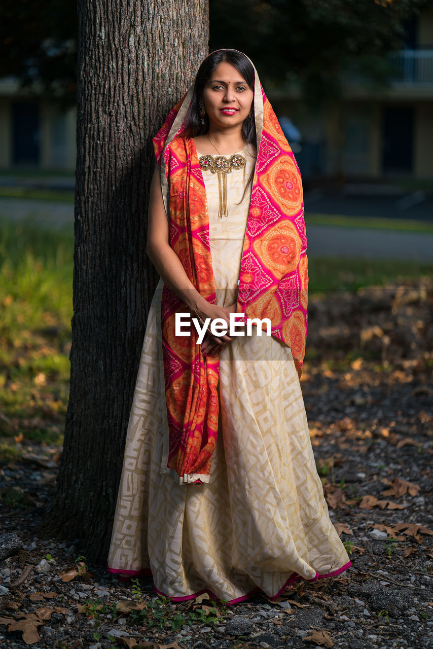 Portrait of young woman in traditional clothing standing against tree trunk