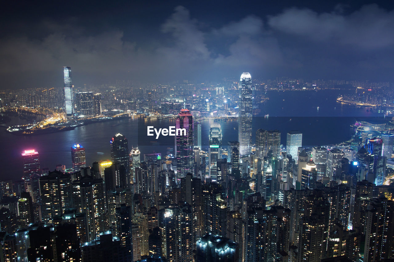 Illuminated cityscape at victoria harbour against sky