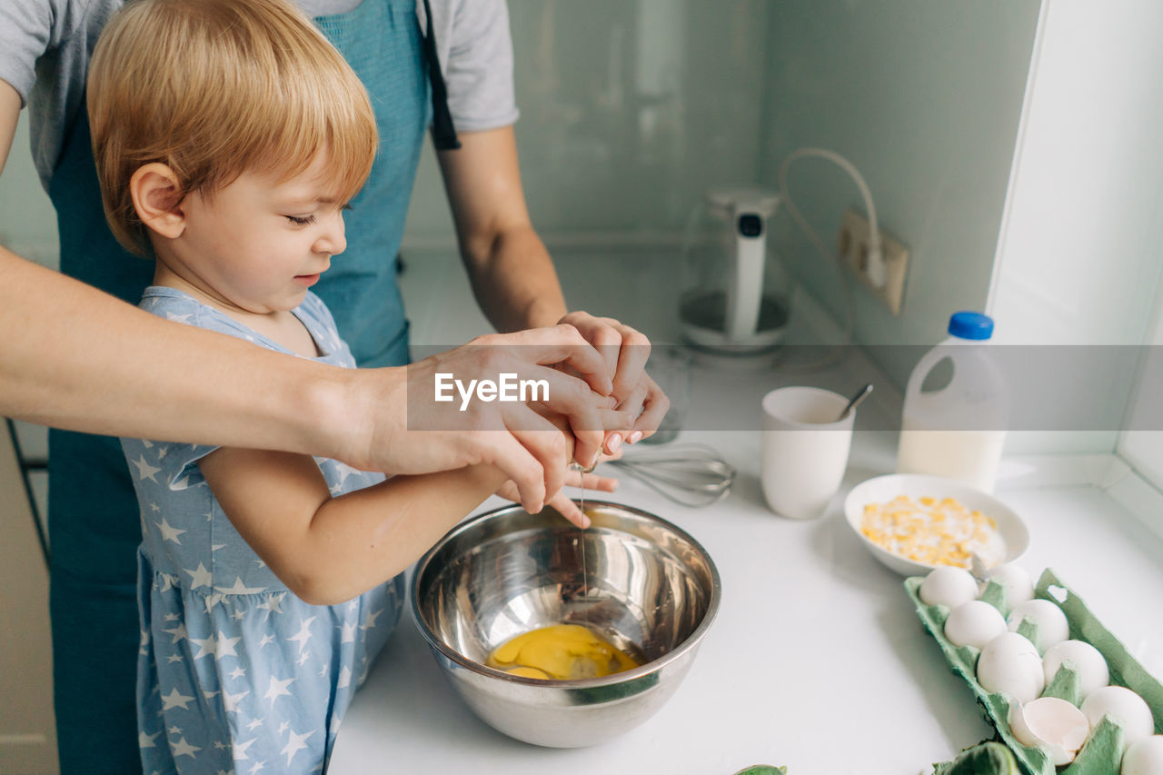 Mom teaches her daughter to break eggs into a bowl for cooking dinner.