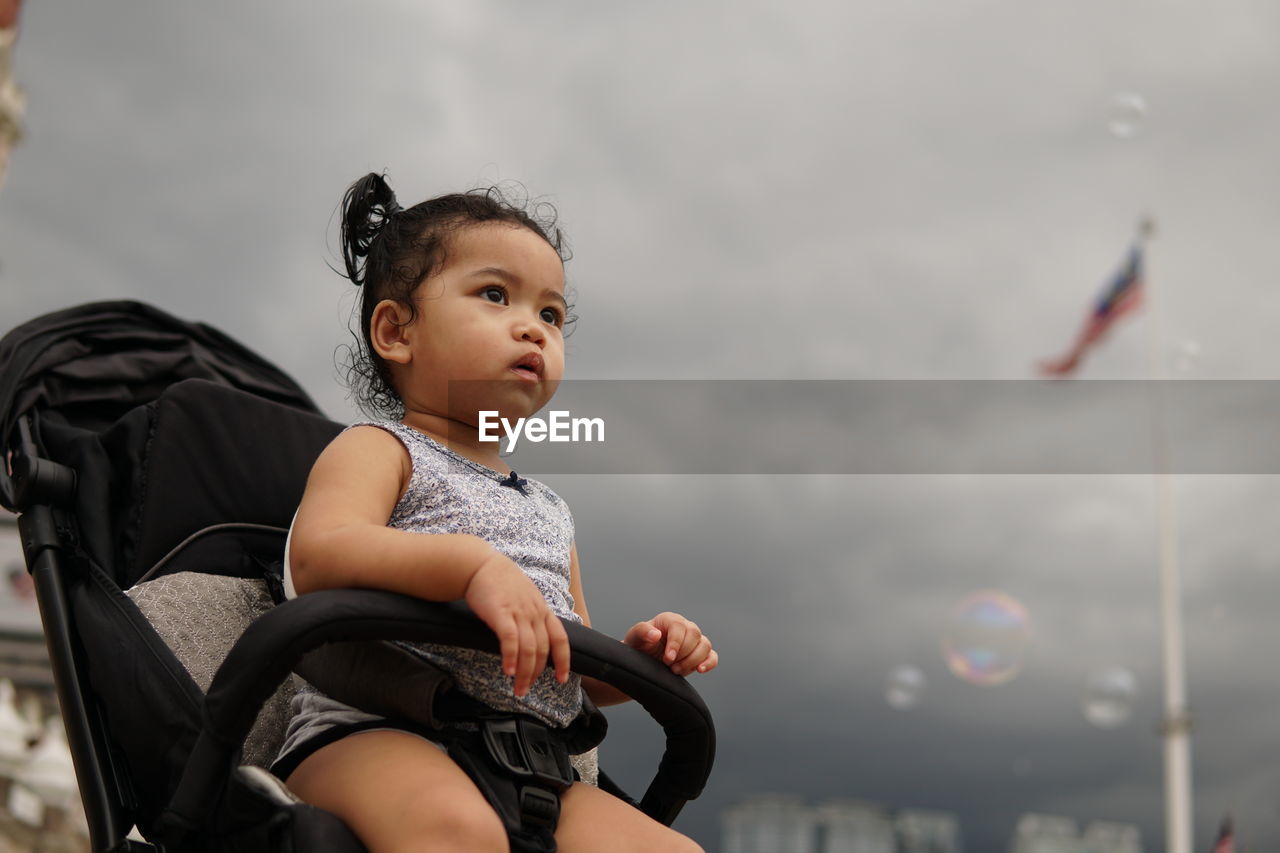 Close-up of cute smiling girl sitting outdoors against sky