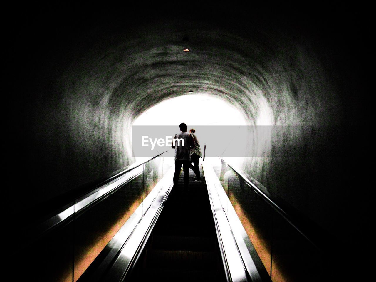 REAR VIEW OF SILHOUETTE PEOPLE STANDING IN TUNNEL