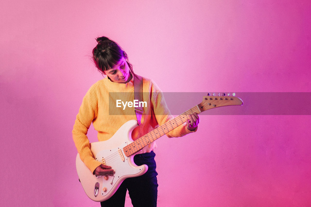 Woman playing guitar against pink background