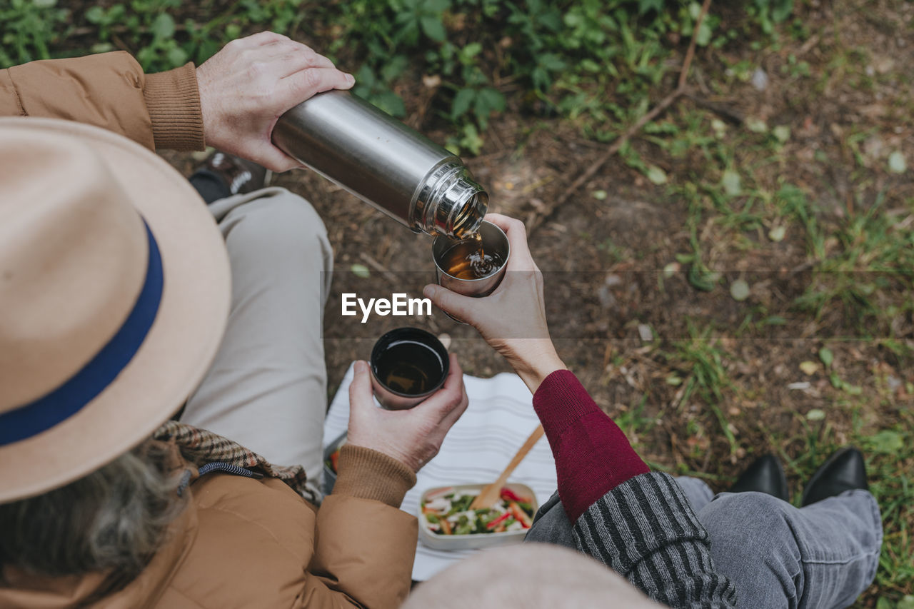 Man pouring hot tea from thermos to woman in forest