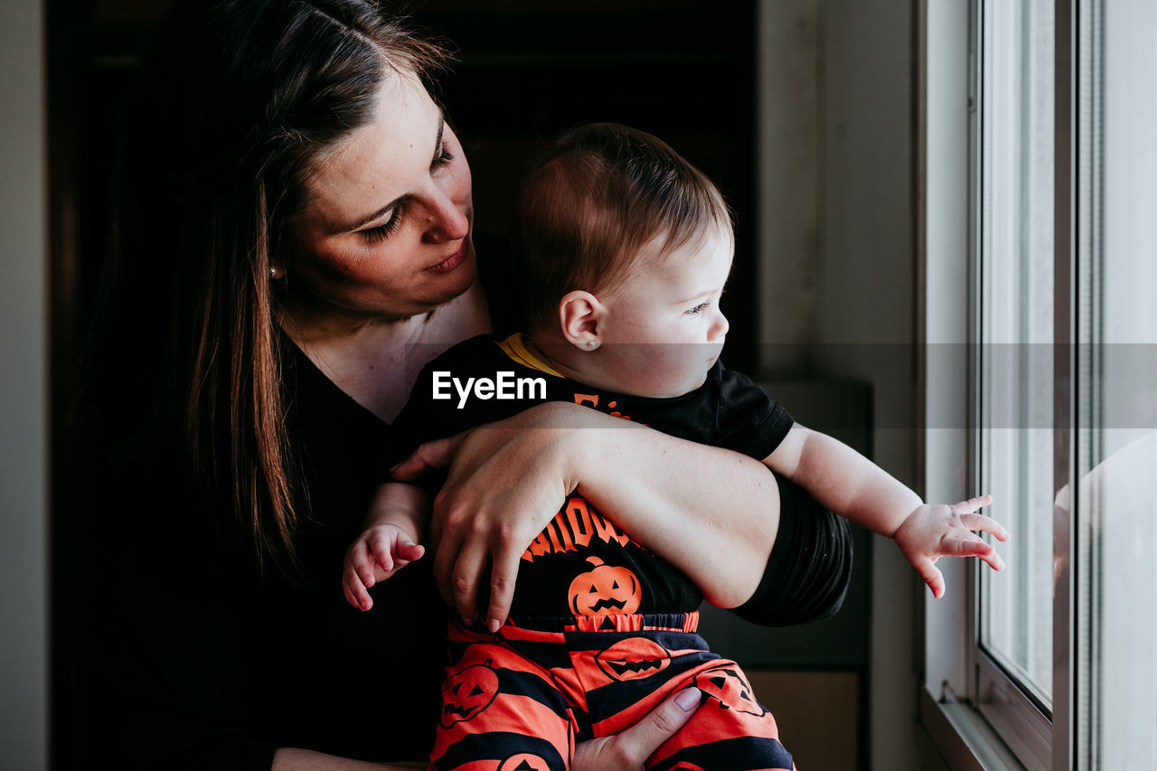 Smiling mother holding daughter sitting by window at home