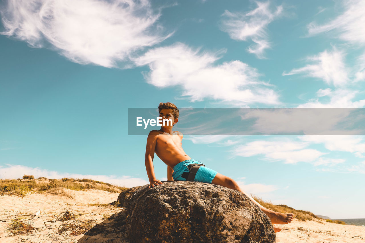 FULL LENGTH OF SHIRTLESS MAN SITTING ON ROCK