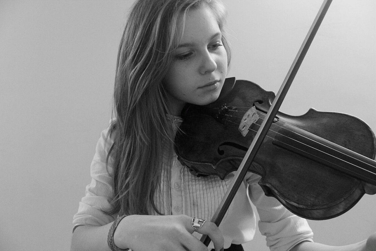 Woman playing violin while standing against wall