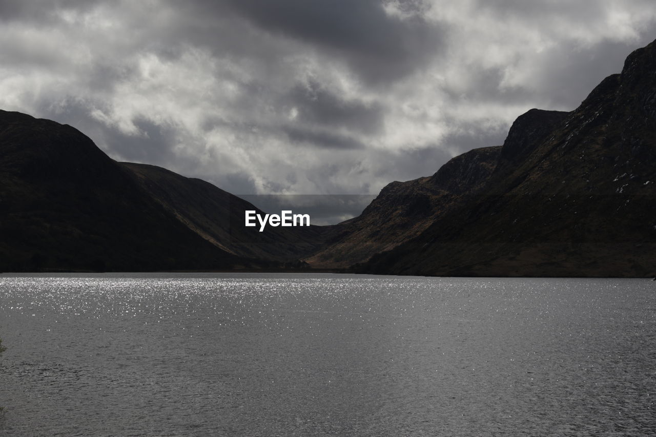 mountain, cloud, lake, scenics - nature, sky, water, environment, landscape, mountain range, highland, beauty in nature, nature, no people, land, horizon, dramatic sky, tranquility, tranquil scene, overcast, travel destinations, reflection, non-urban scene, outdoors, dramatic landscape, travel, storm, coast, monochrome, black and white, storm cloud