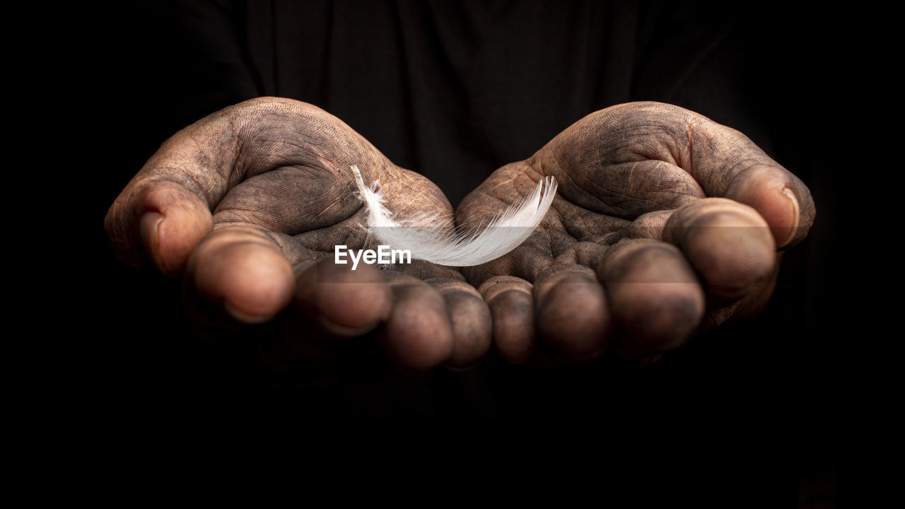 Cropped image of messy hands holding feather against black background