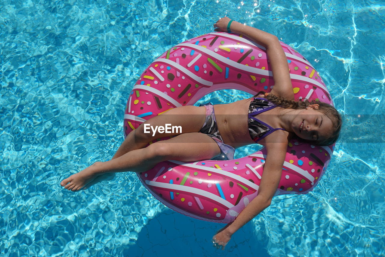 High angle view of girl lying inflatable ring on swimming pool