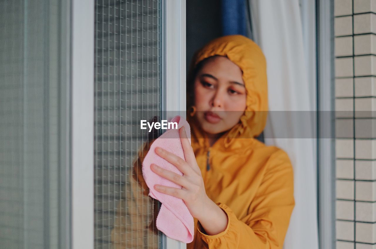 Portrait of young woman standing against window