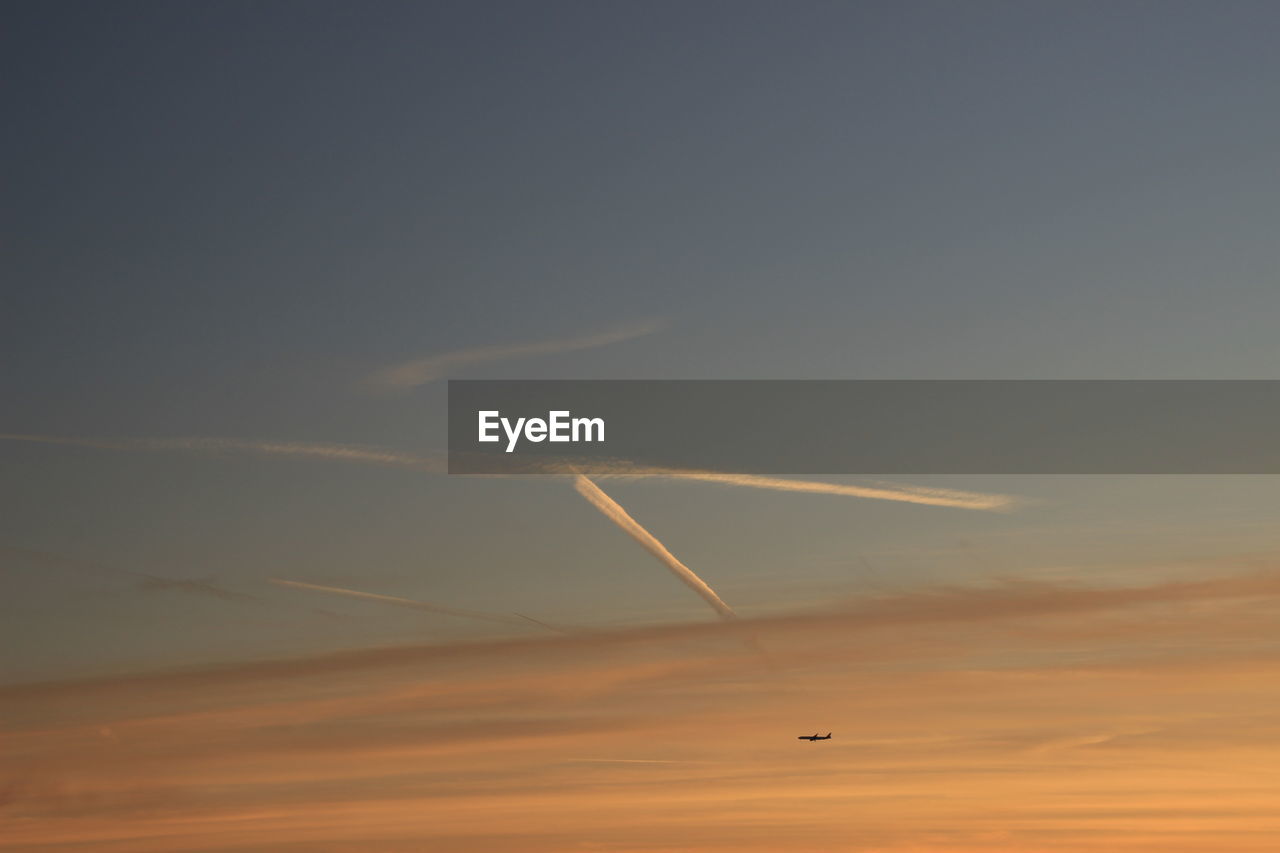 Low angle view of airplane performing smoke stunt during sunset