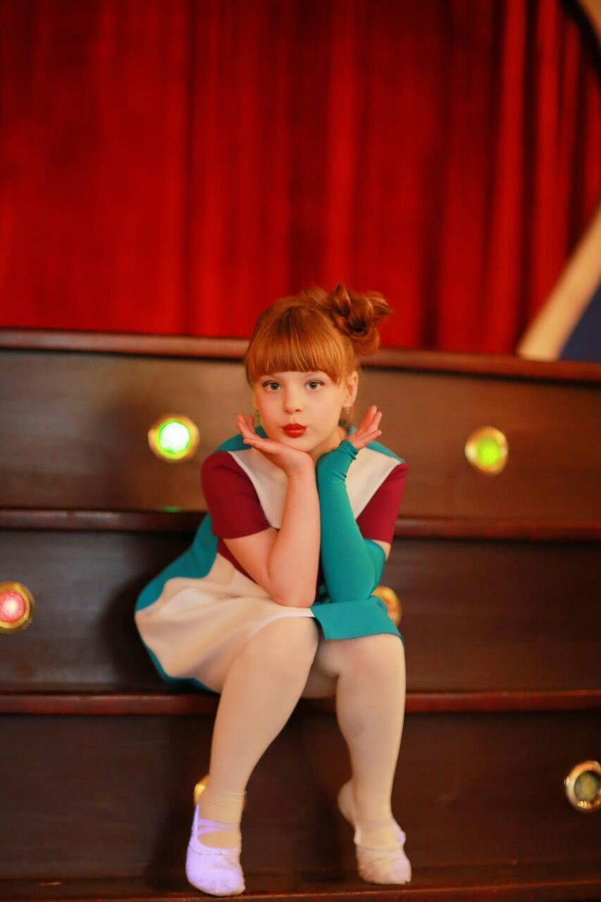 Portrait of ballet dancer sitting on wooden stage steps at theatre