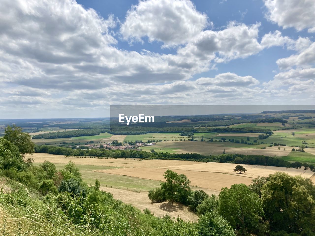 landscape, environment, plant, sky, scenics - nature, land, plain, cloud, nature, field, rural area, beauty in nature, hill, tree, rural scene, agriculture, horizon, grass, grassland, tranquility, tranquil scene, green, no people, non-urban scene, day, growth, outdoors, farm, natural environment, travel, plateau, horizon over land, prairie, sunlight, travel destinations, idyllic, blue, high angle view, tourism, pasture, crop, summer, water, cloudscape, architecture, building