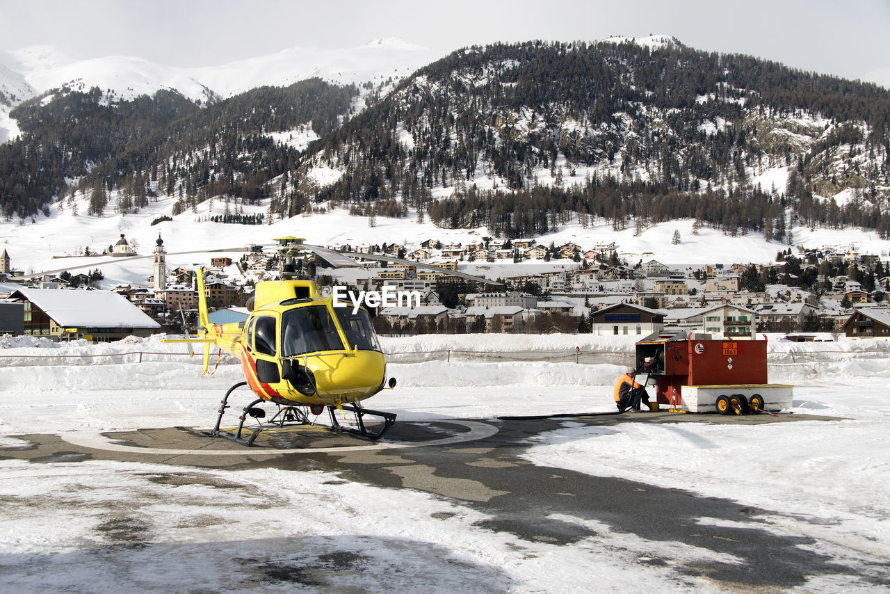 A yellow tour helicopter getting fuel in heliport in the alps switzerland in winter