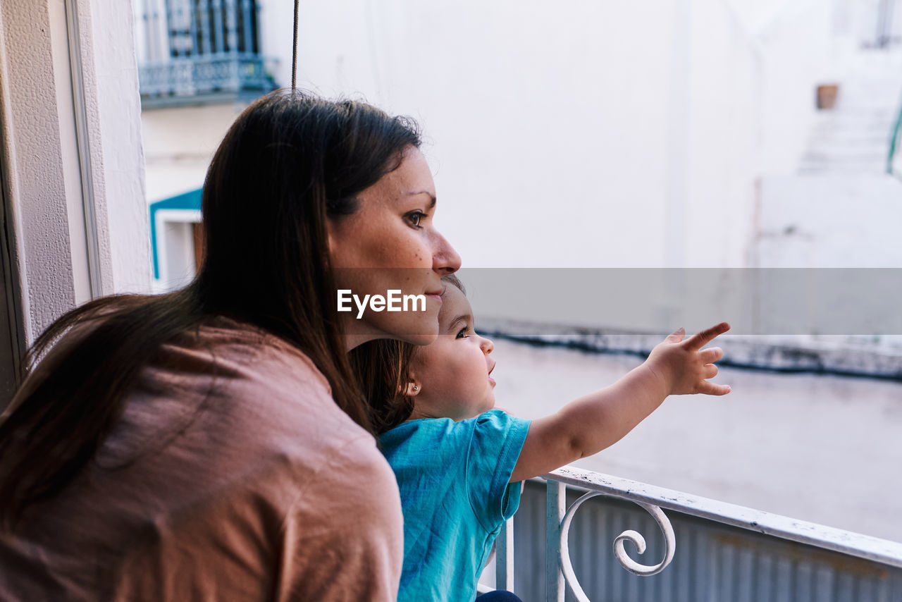 Mother and daughter looking out the window of the house happy