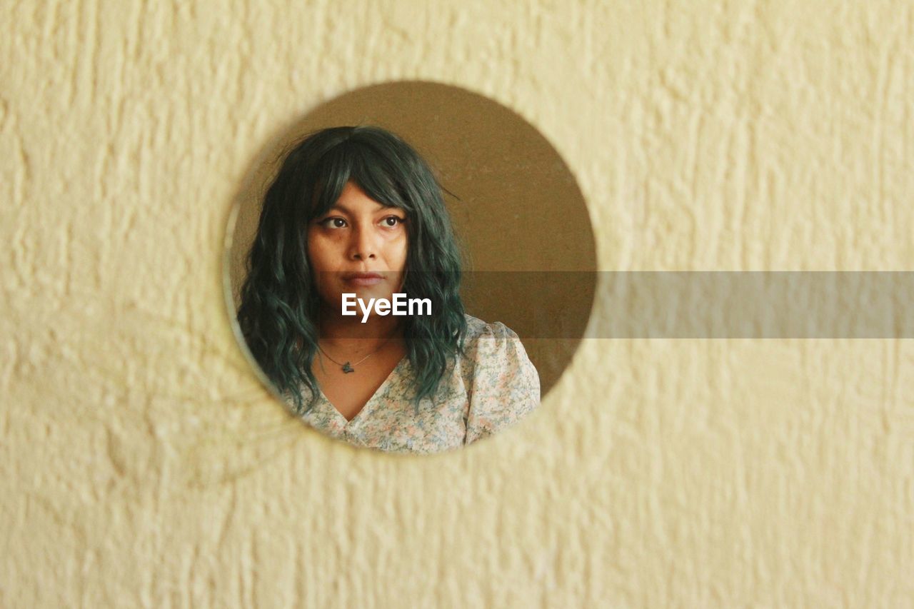 Portrait of young woman standing against wall