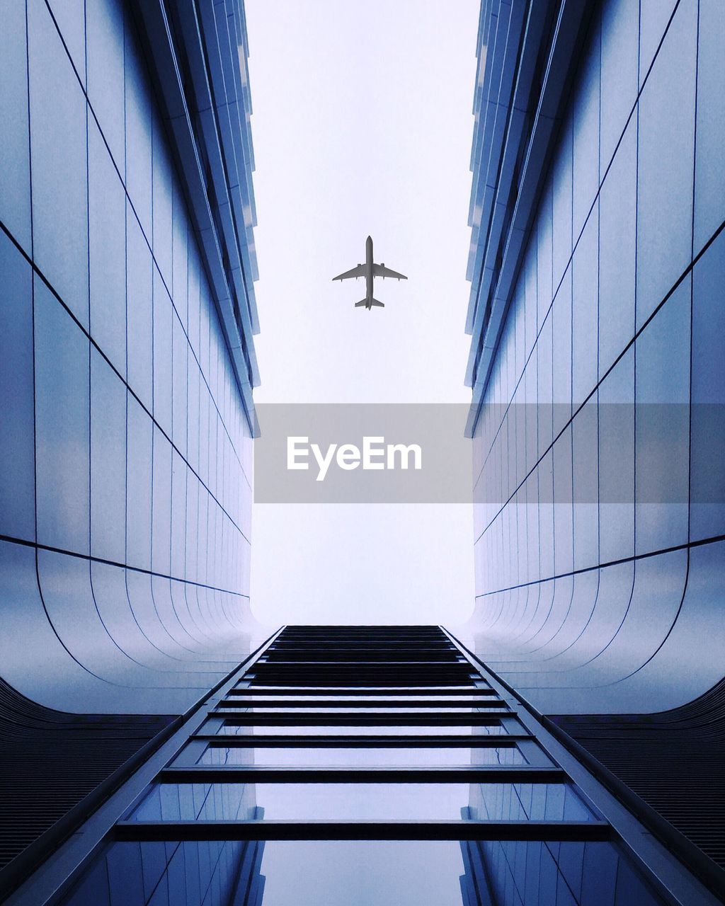 Low angle view of modern building against airplane flying in clear sky