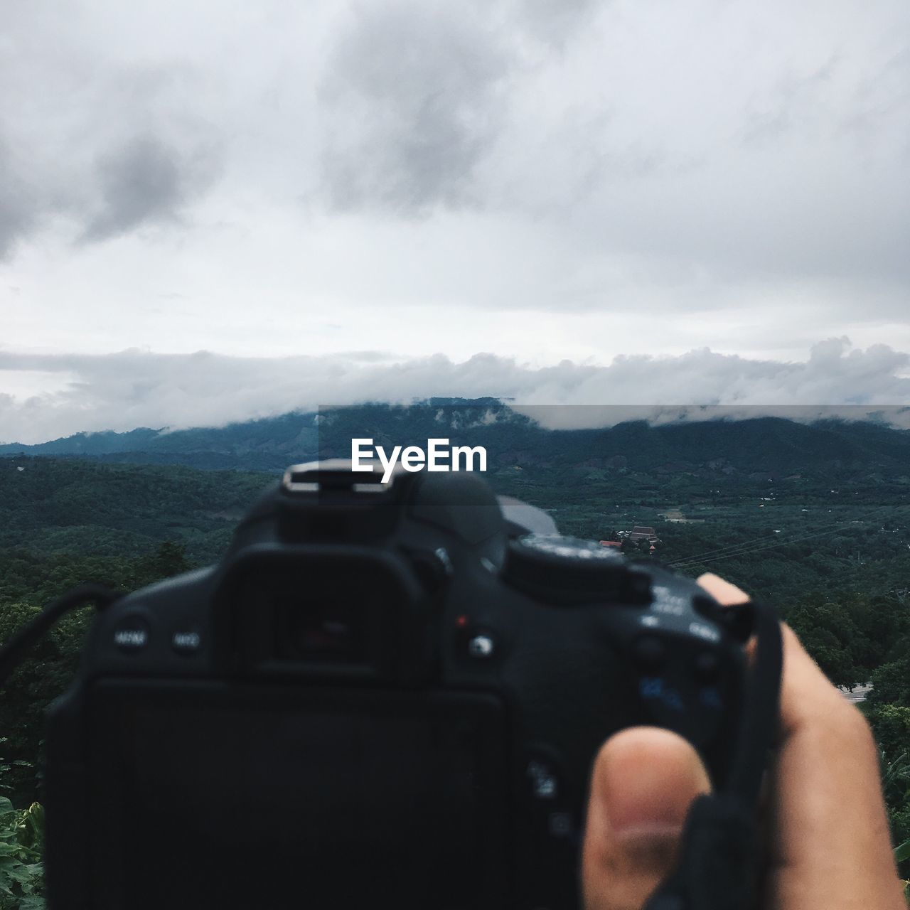 Cropped hand holding camera against sky