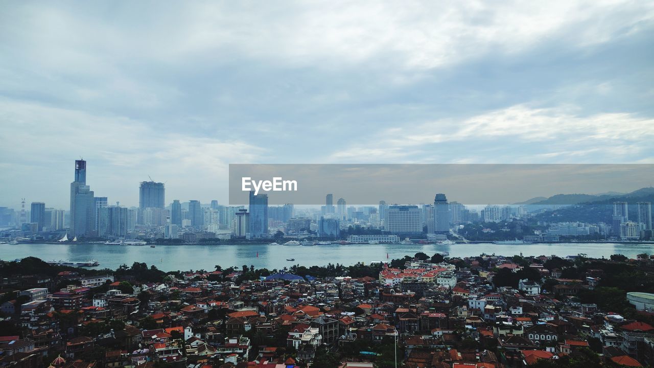 City at waterfront against cloudy sky