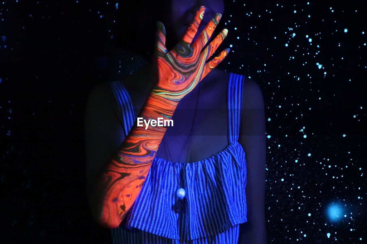 Midsection of woman with multi colored hand standing against illuminated lights at night