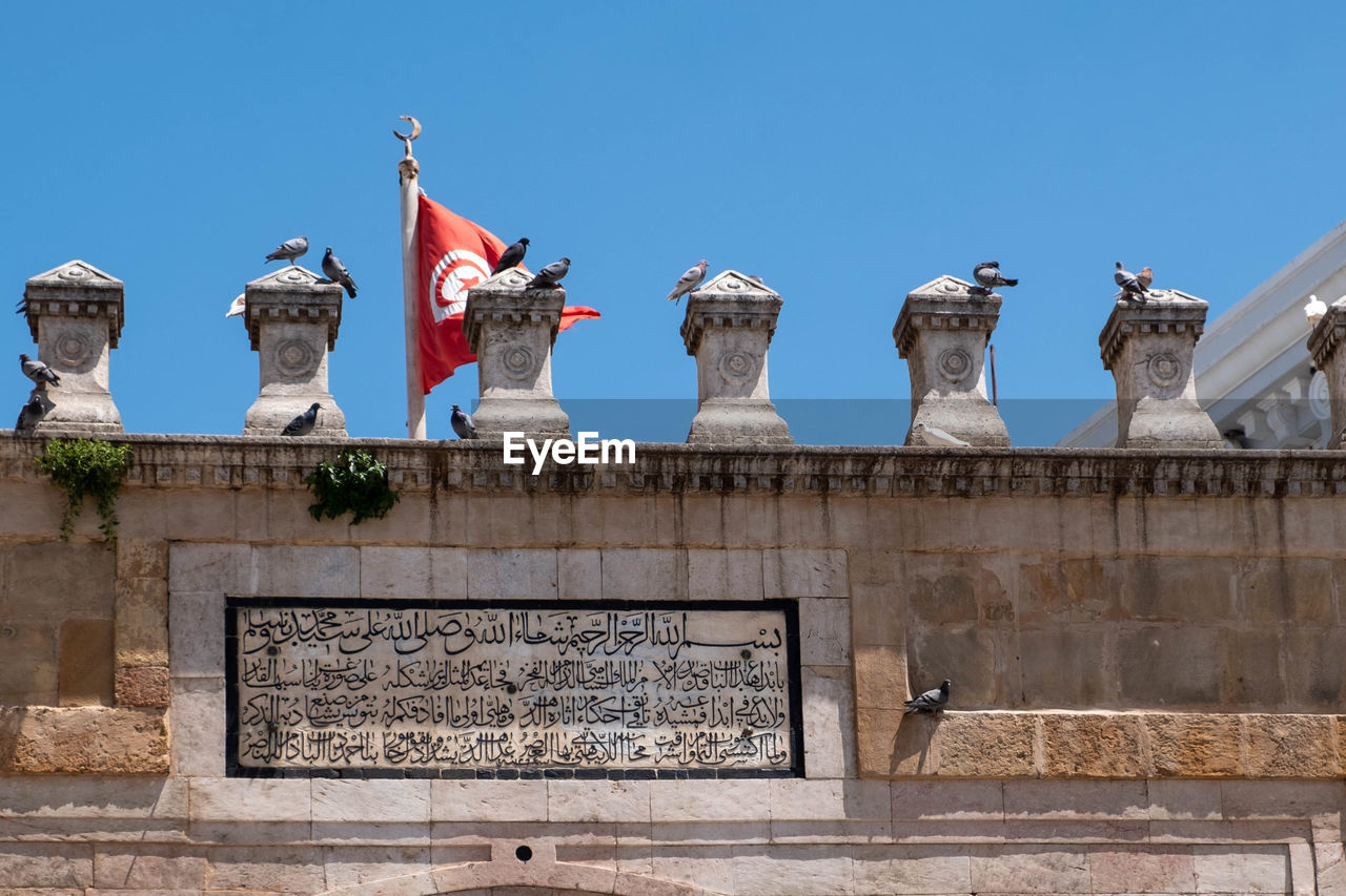 architecture, ancient history, clear sky, built structure, monument, sky, history, the past, no people, building exterior, blue, landmark, travel destinations, nature, day, wall, flag, sunny, tourism, statue, travel, temple, outdoors, city, sculpture, craft, building, low angle view, memorial, representation