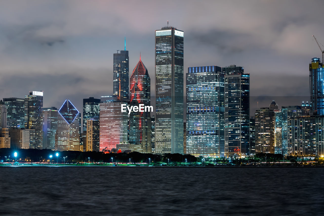 Sea by illuminated buildings against sky