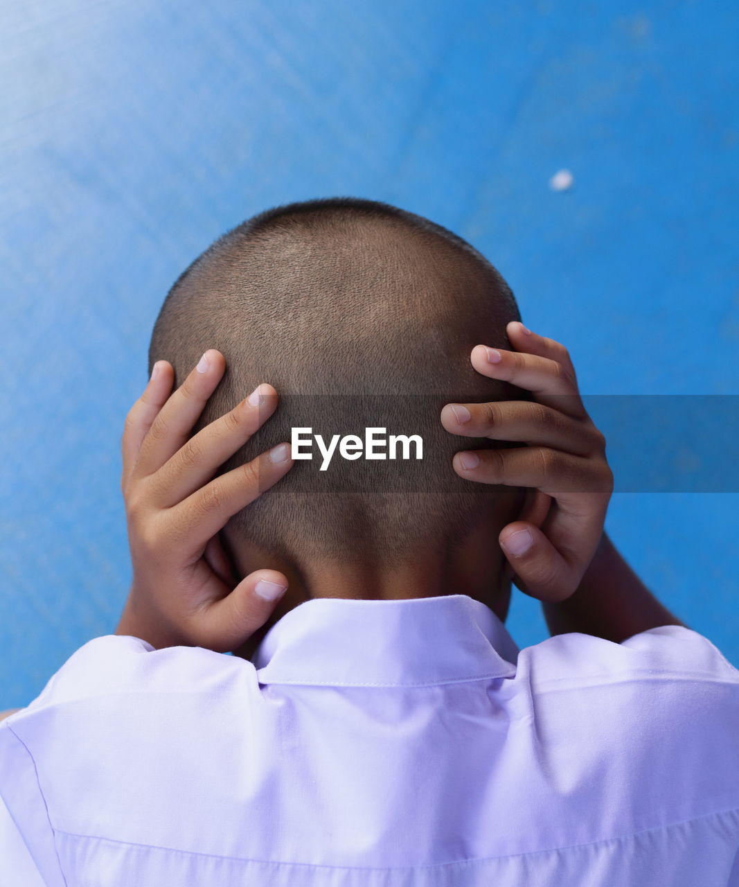 Rear view of boy covering ears against blue wall