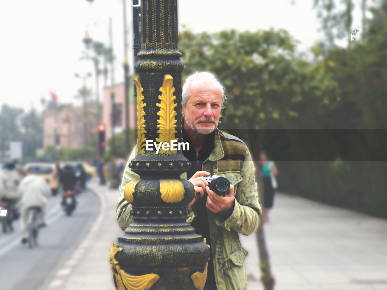 Portrait of senior man with camera in city against sky