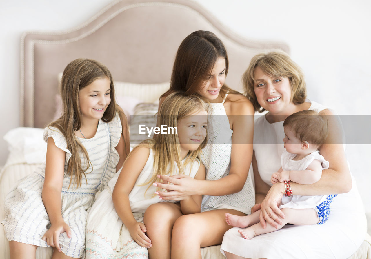 Cheerful mothers with kids sitting on bed at home