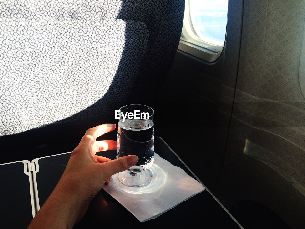 Cropped hand reaching for drinking glass by airplane window