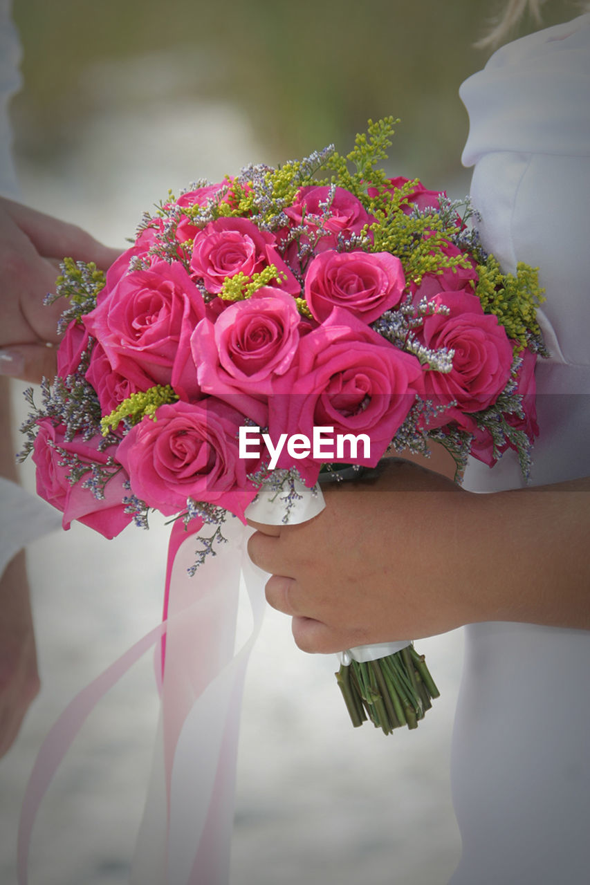 Midsection of bride holding rose bouquet at wedding