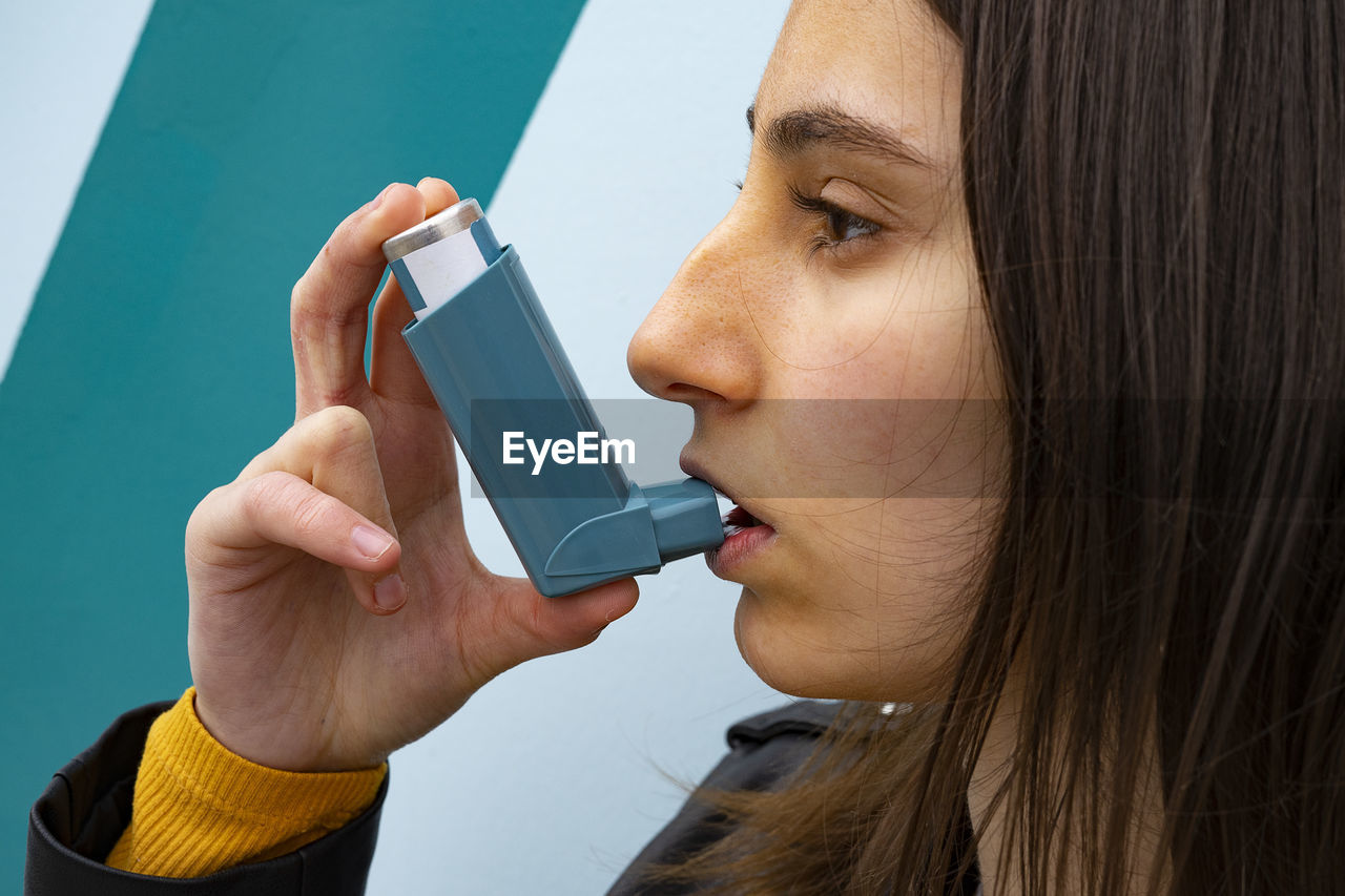 Woman inhaling a blue asthma inhaler on a blue background.