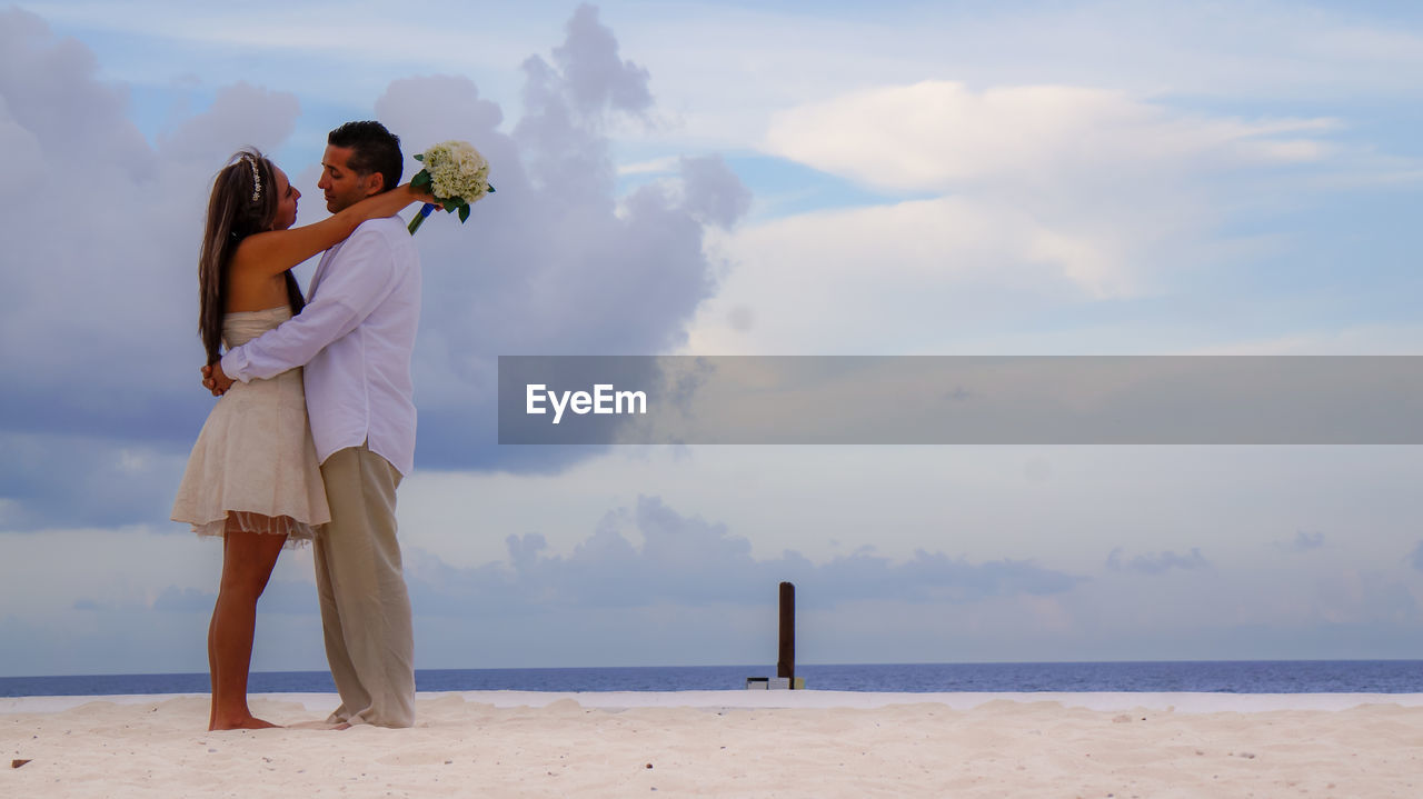 COUPLE STANDING ON BEACH AGAINST SKY